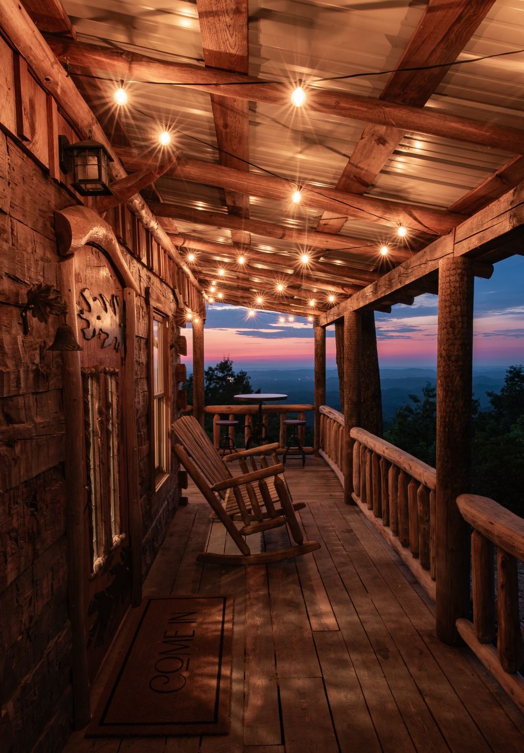 Log cabin porch with string lights and rocking chair at sunset